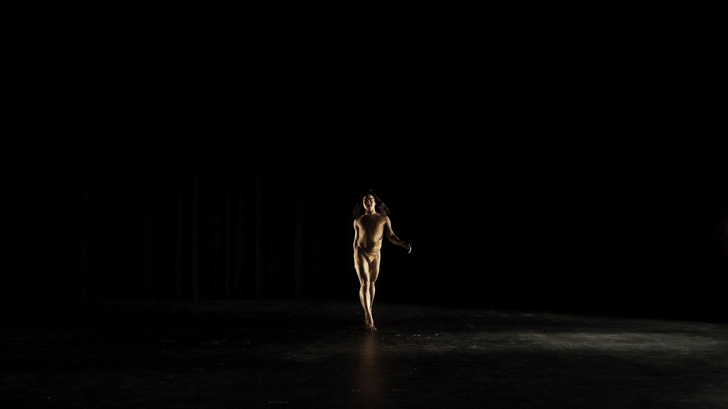 a dance walks towards the camera in a darkened space