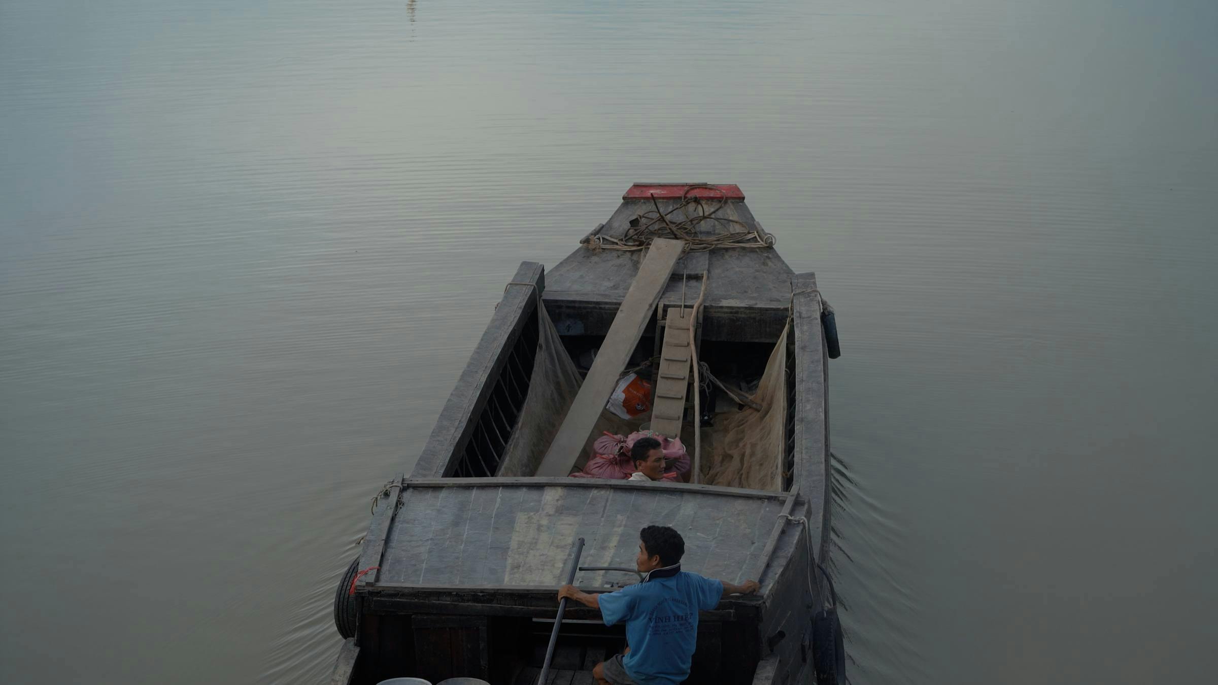Image of an open top boat floating across grey water which has two people inside.
