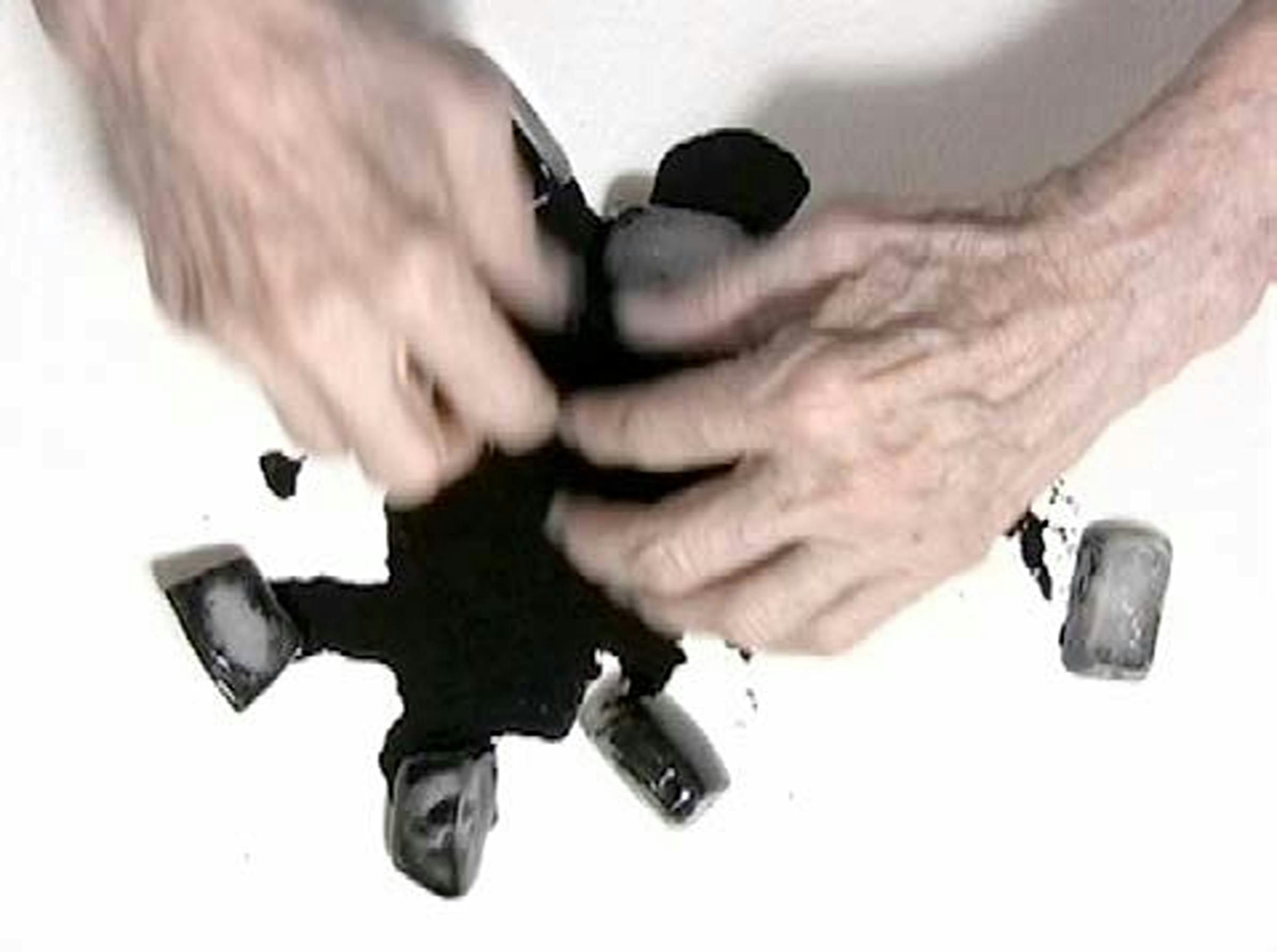 The artist's hand hold ice cubes and move around black ink on a white surface