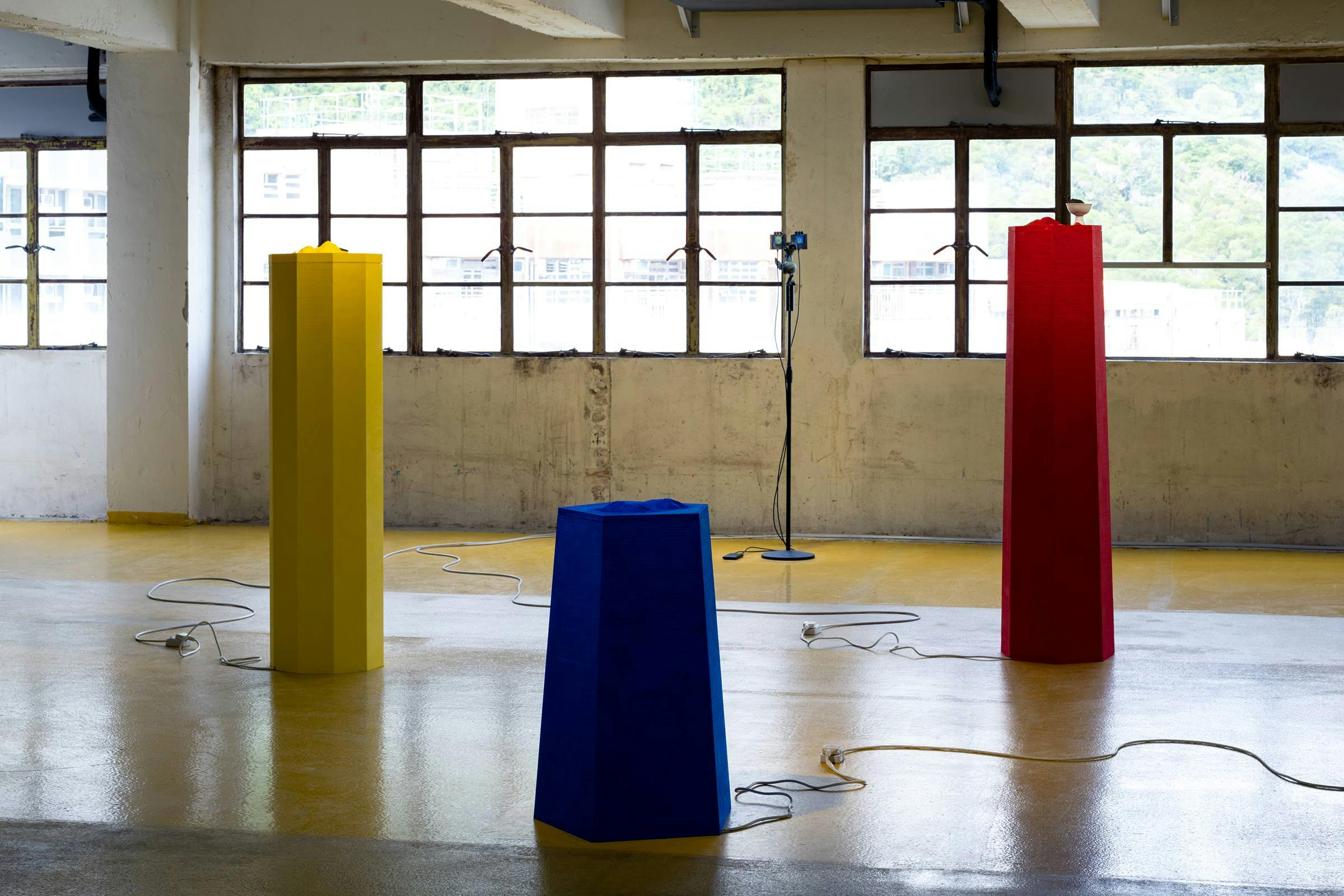 Installation view, Samson Young, The messengers from Music for selective hearing, or assisted living, 24 September - 5 November 2022, Kiang Malingue, Hong Kong. Multiple art works are visible in an industrial space that has a yellow floor