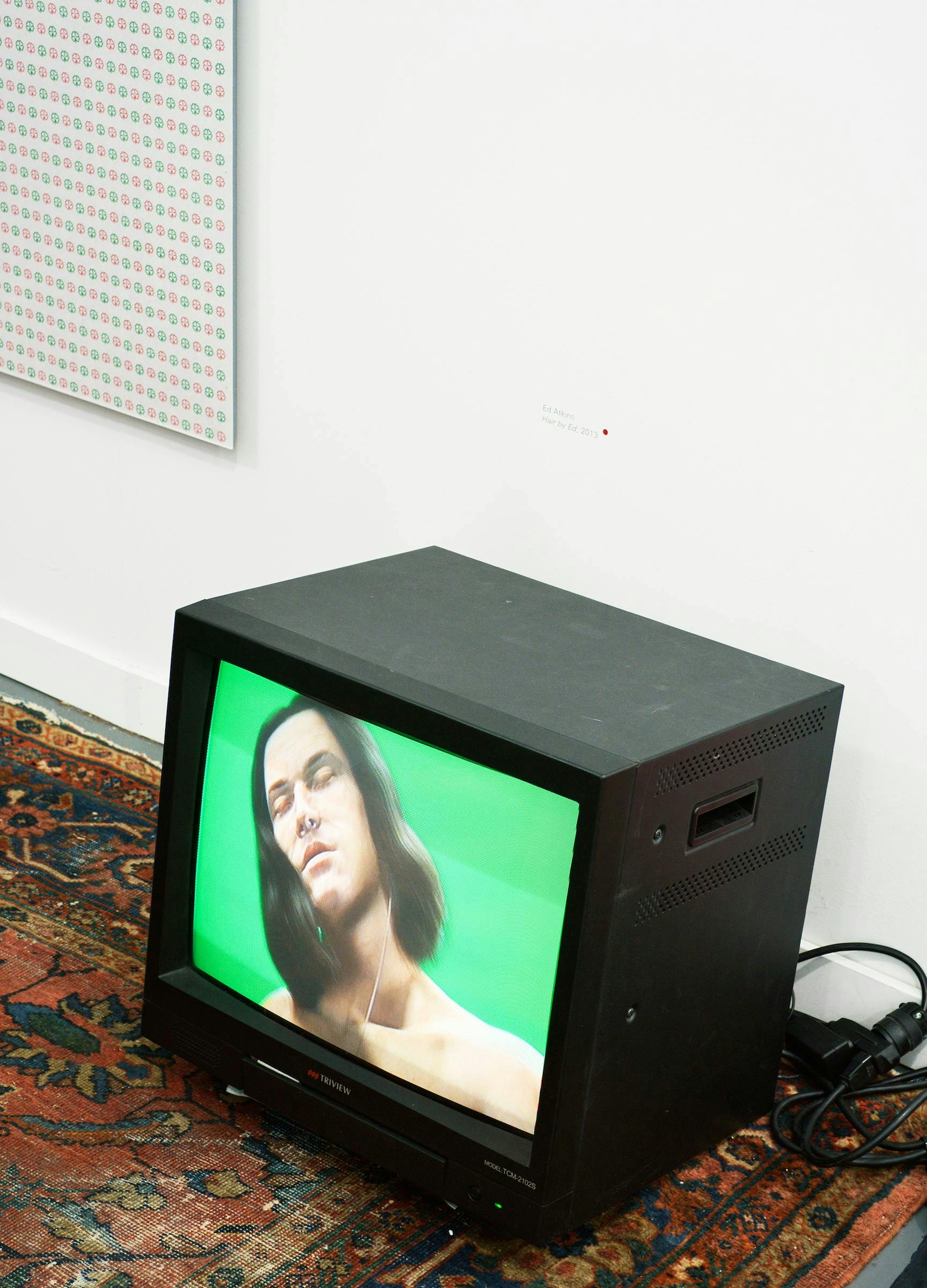 an installation image of Hair by Ed by Ed Atkins. The work is installed on a hantarex monitor and is sitting directly on a patterned carpet