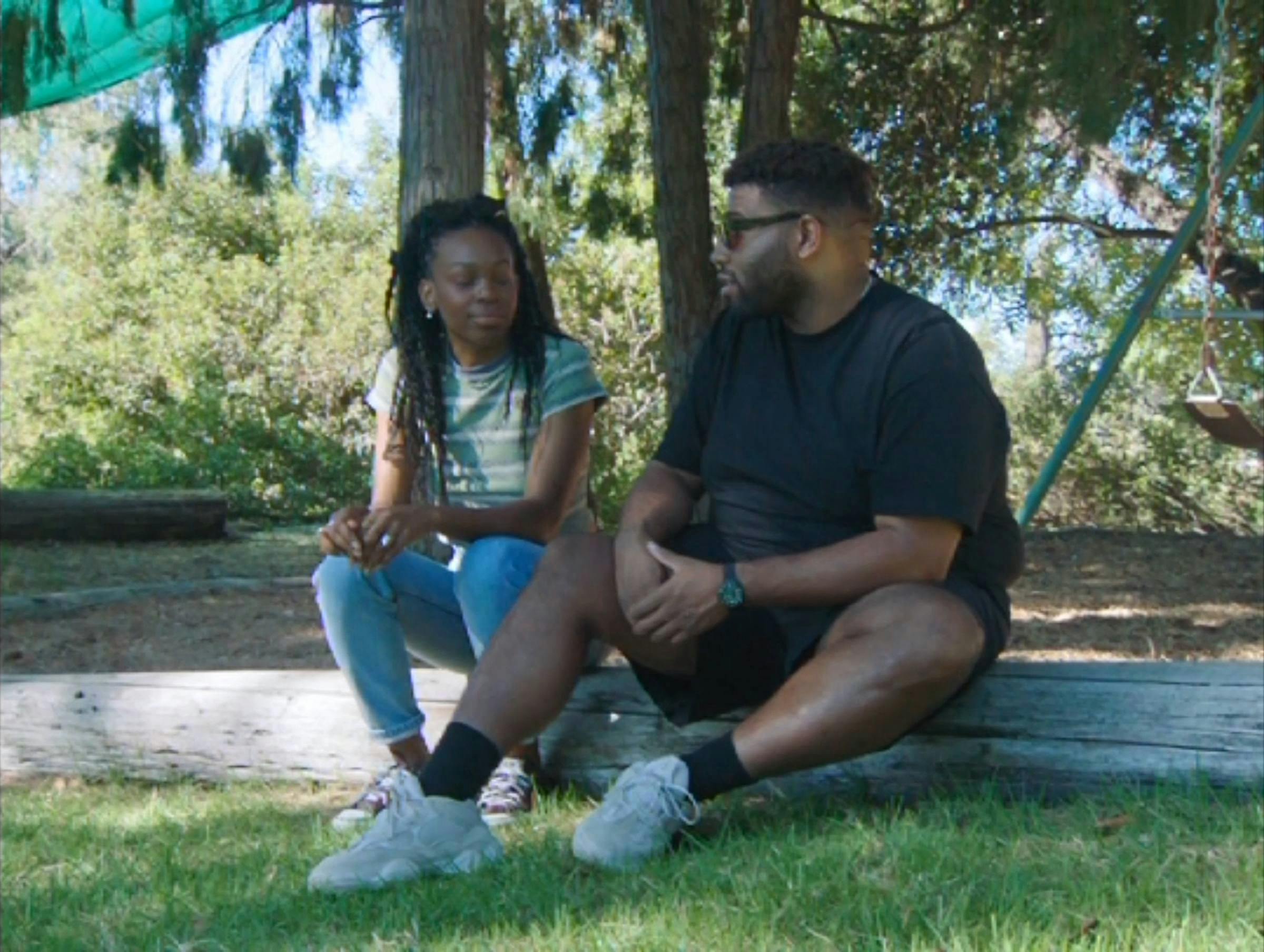 two young black people it next to each other in a park