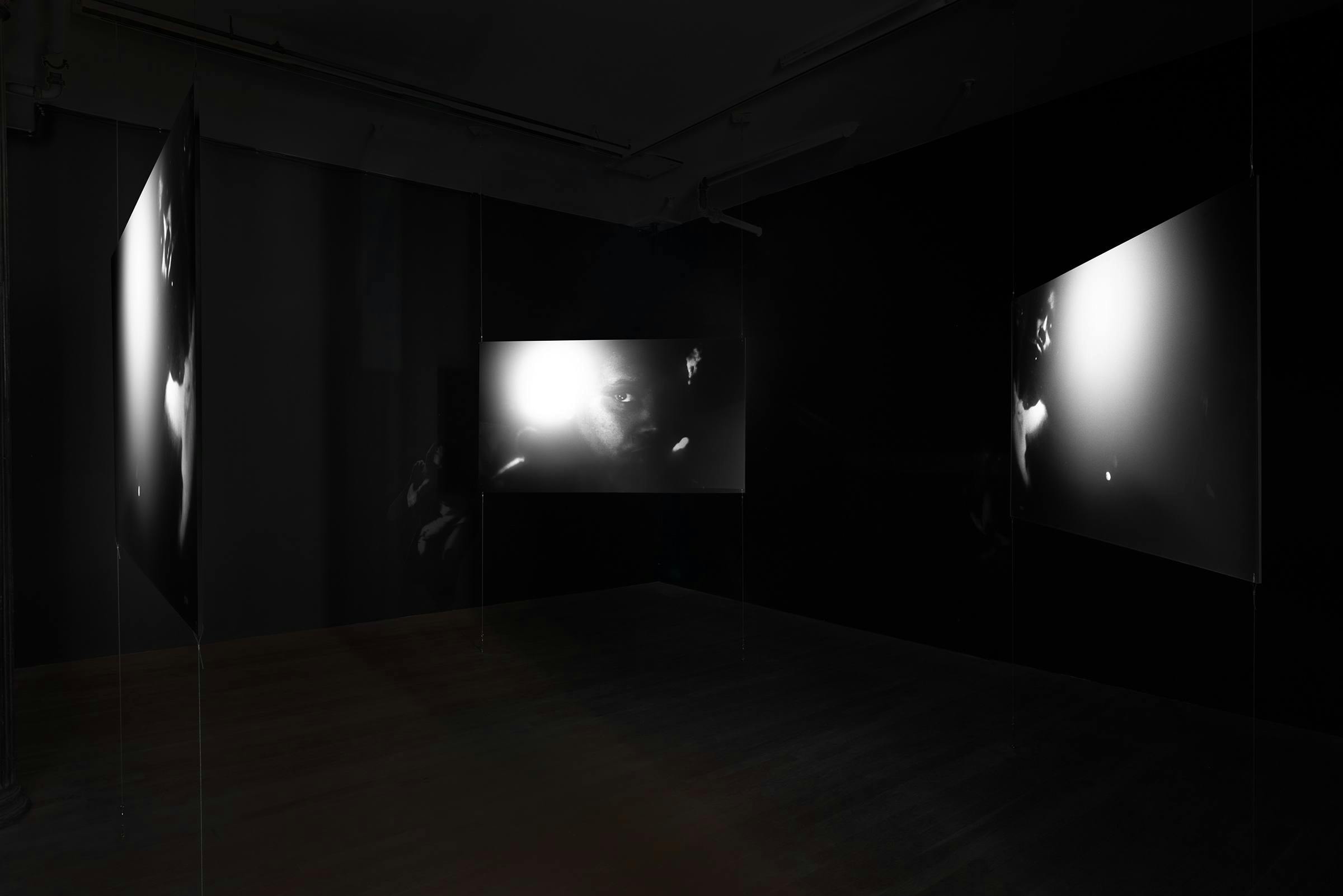 Three monochrome projection panels float equidistantly in a dark room.