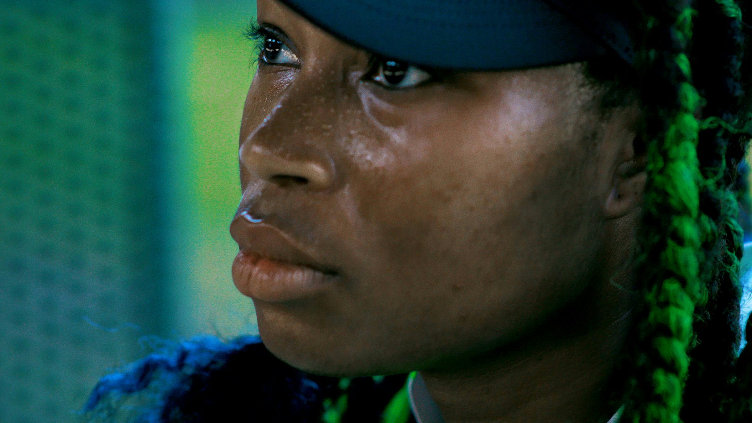 A close up of the artist's face. She has green hair and is wearing a black cap