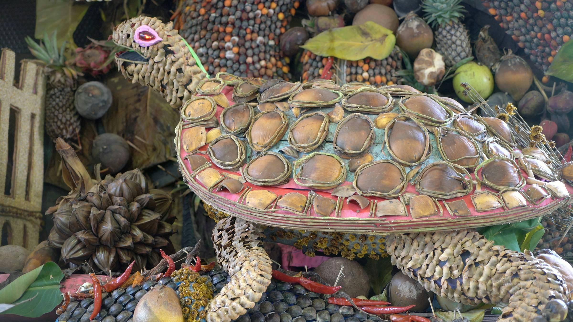 Image of a turtle made out of lots of different stones. The turtle is sat in a setting also made from many different objects such as stones and pineapples.