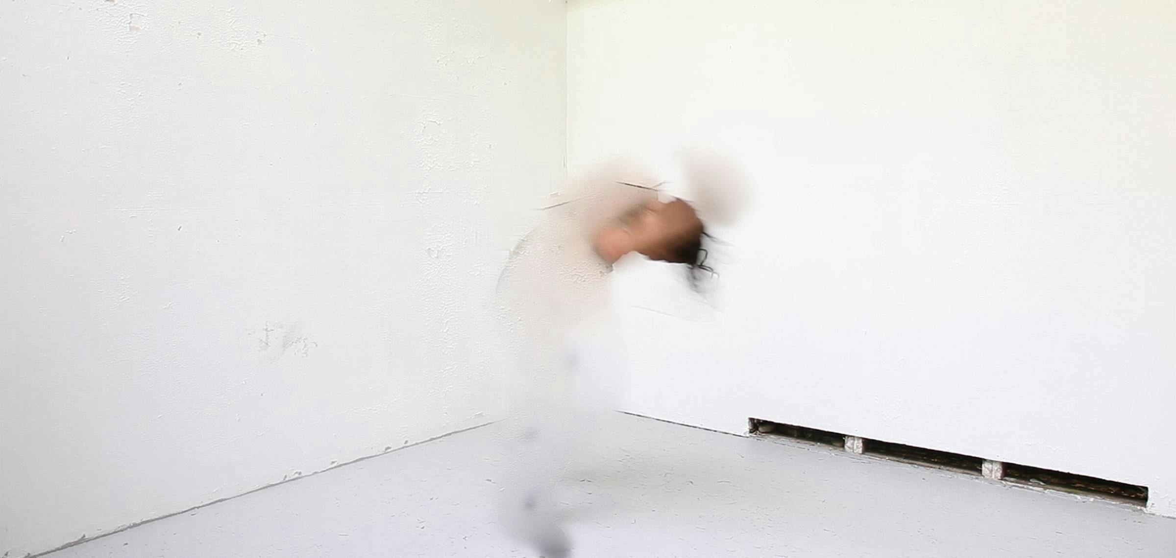 Image of an indistinct figure wearing all white dancing in a white gallery space
