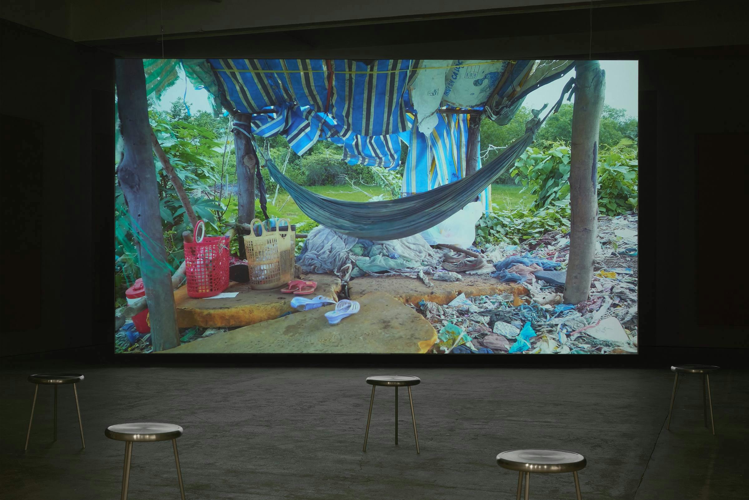 Image of a large projection with stools dotted in front of it in a gallery space.