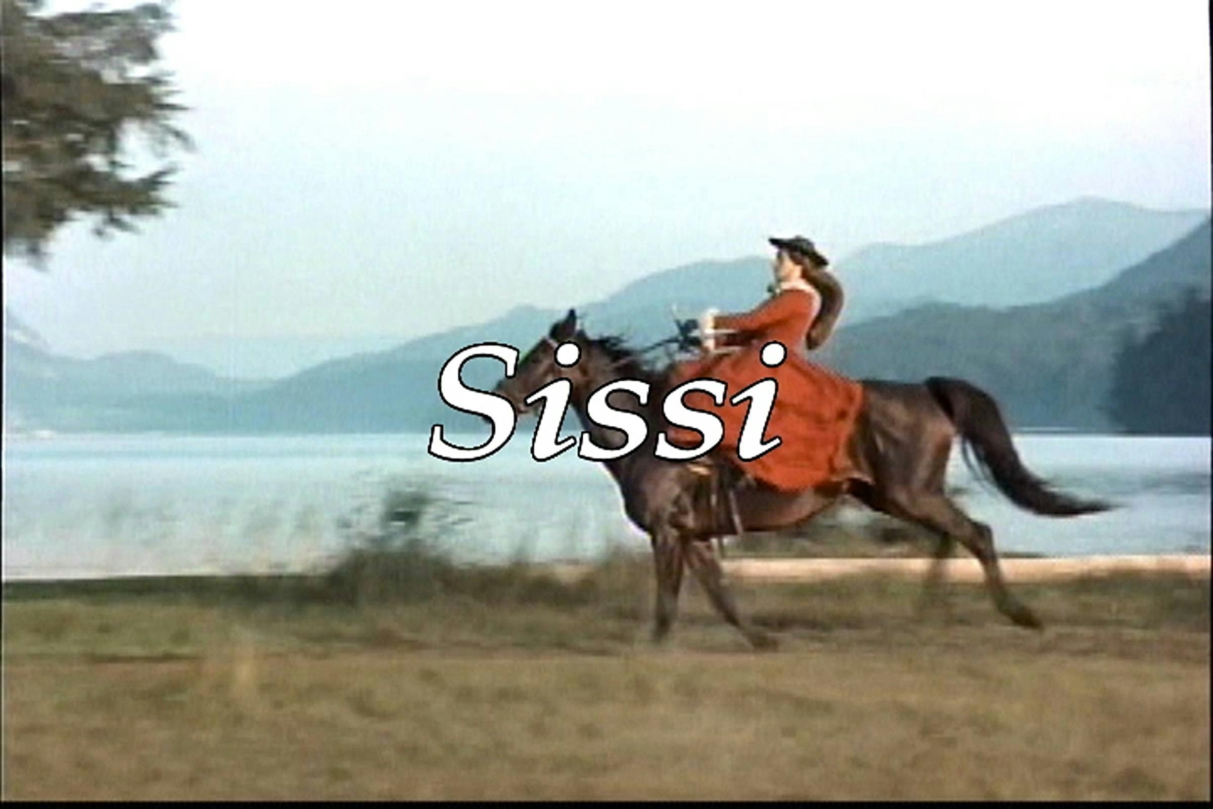Image of someone wearing a red dress riding a horse across a grassy space. The word 'Sissi' is superimposed on top of the image.