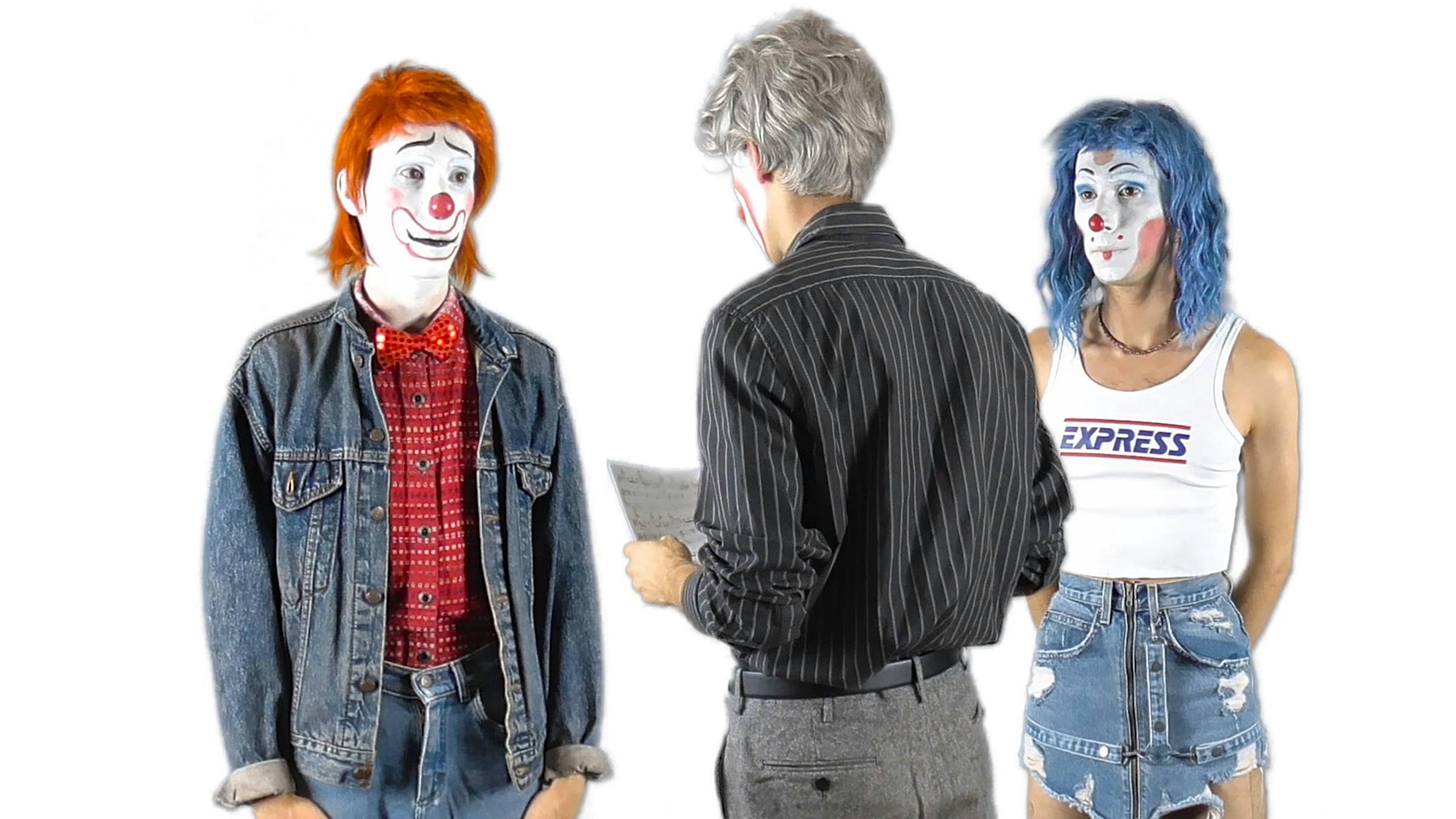Image of three people who each have clown-like makeup painted onto their faces. Two  of the people face the camera and the other has their back turned and is reading from a piece of paper.