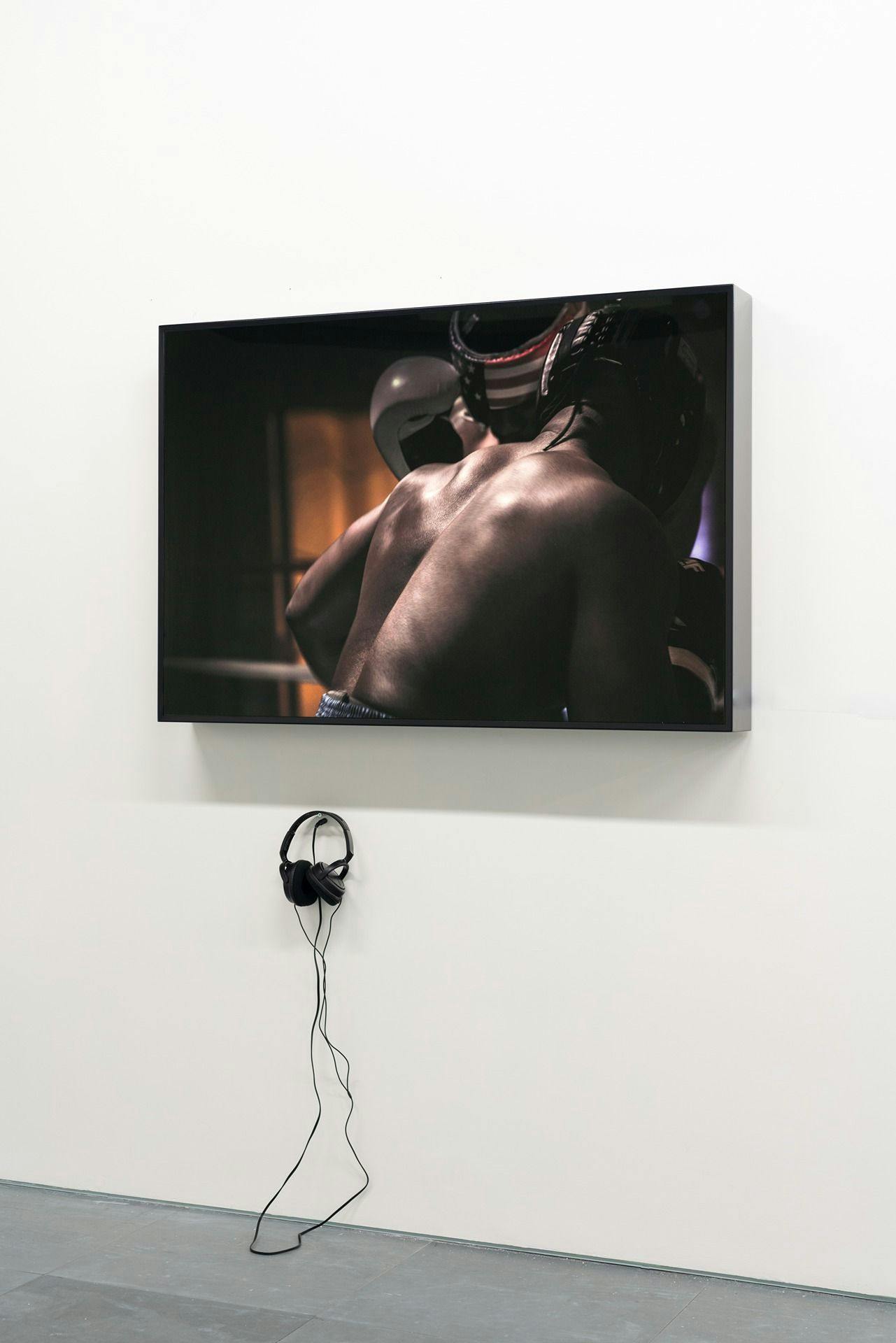 an image of a TV screen where two people are in a boxing embrace. There are headphones underneath the TV screen