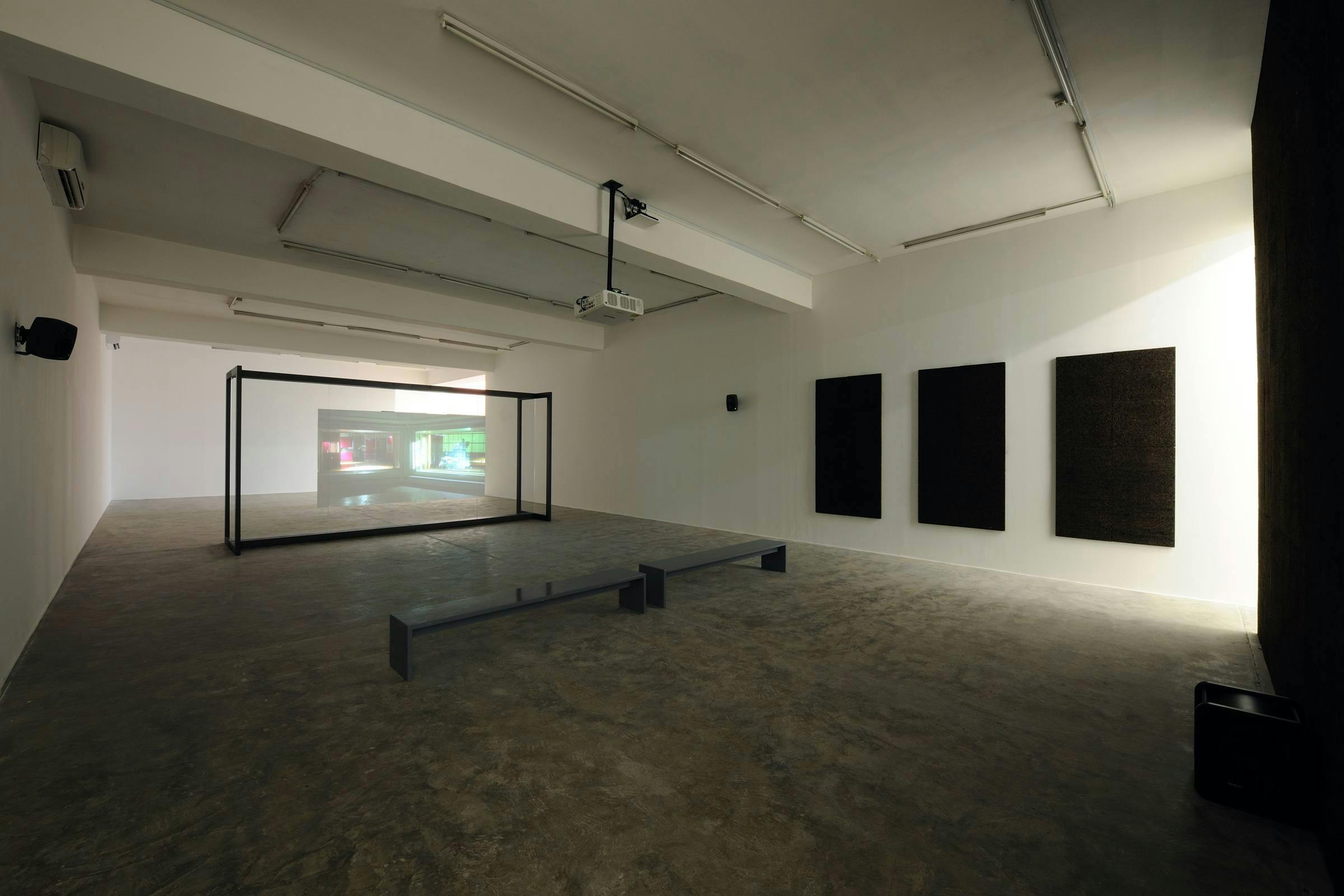A video art work installed in a gallery. There are black sound panels installed on the walls and benches in front of the projection