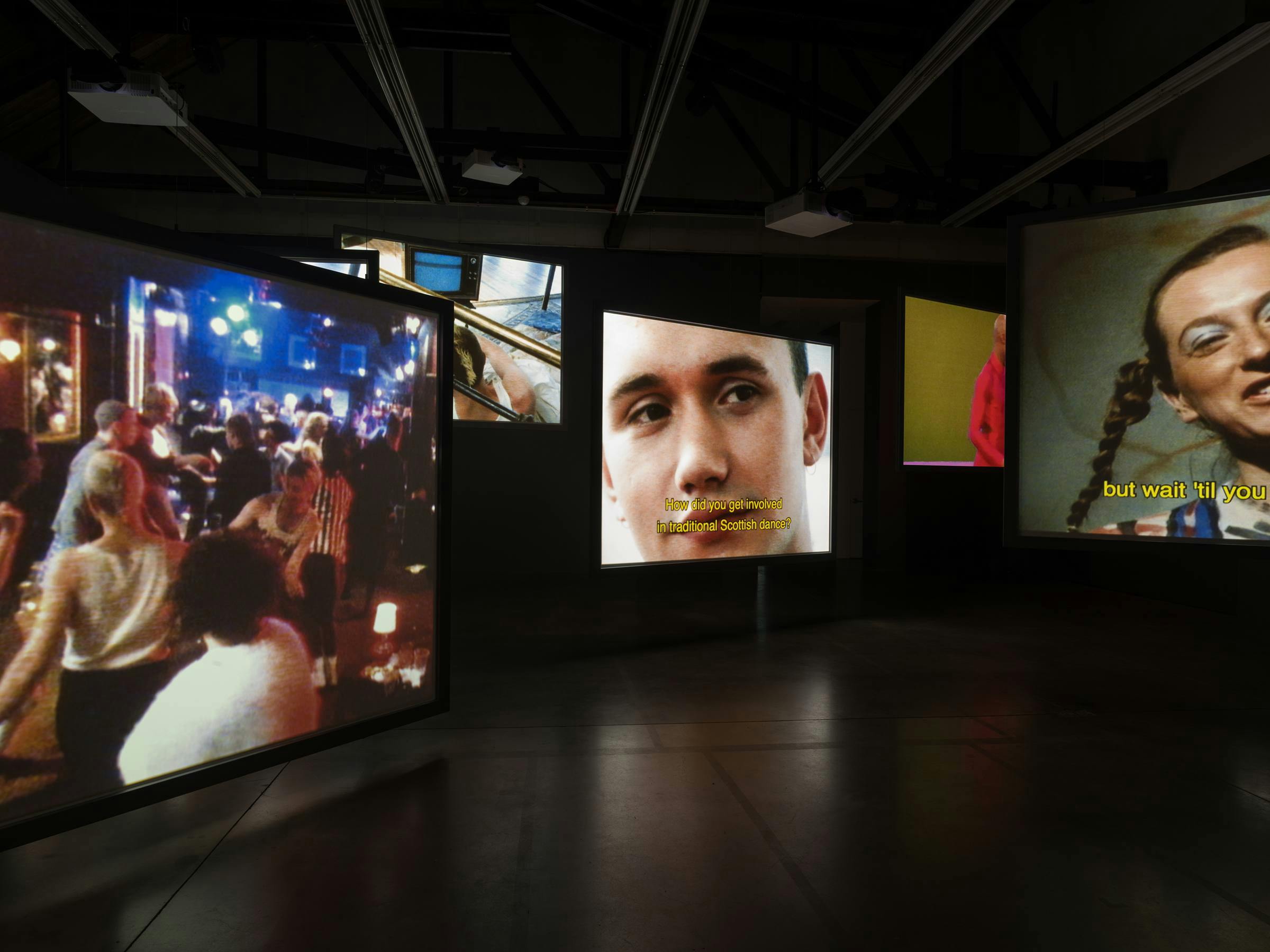 an installation of multiple video works projected on floating screens in a gallery space