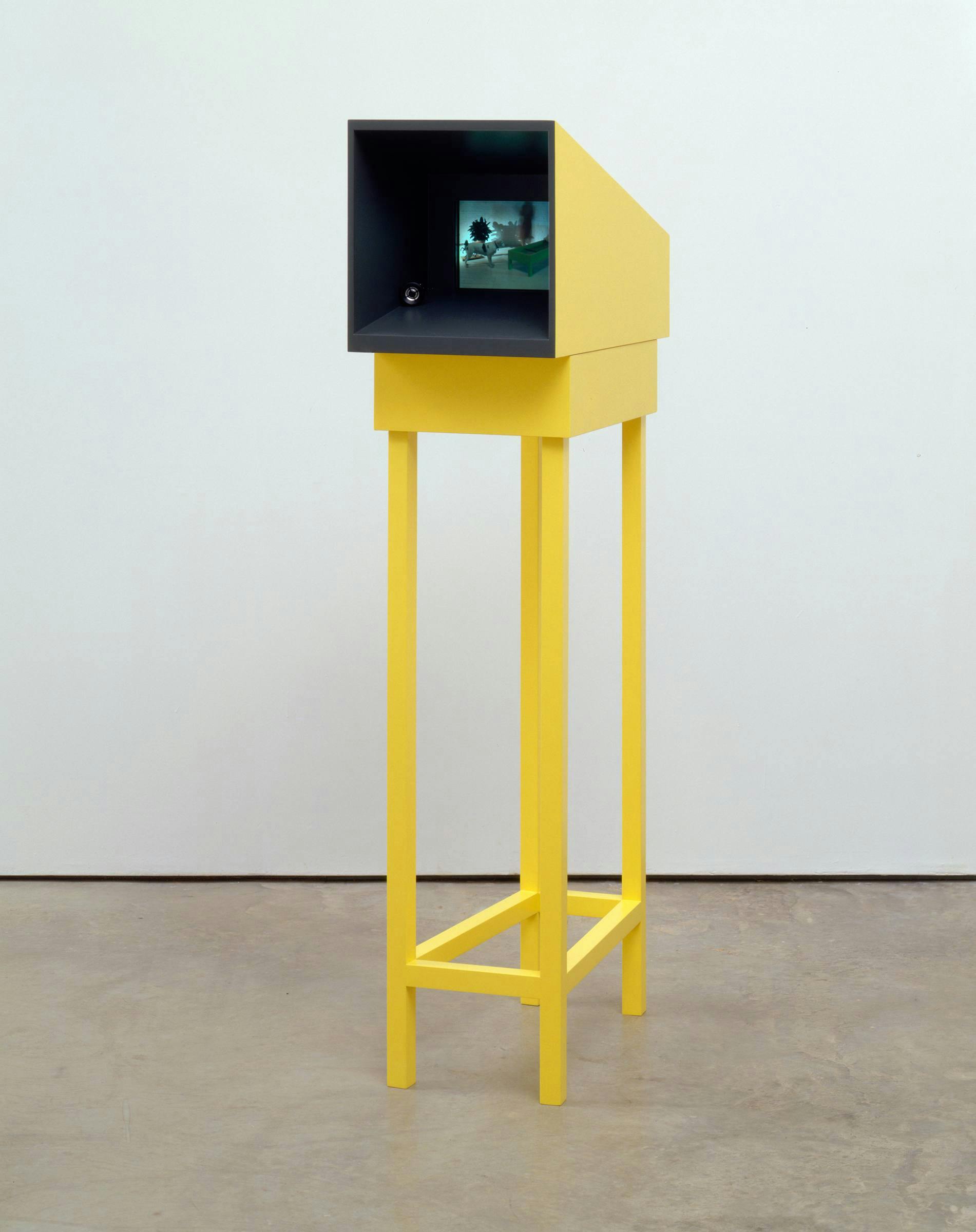 An image of an artwork comprising a yellow projection box on a wooden yellow frame. We can see a film projected inside the box