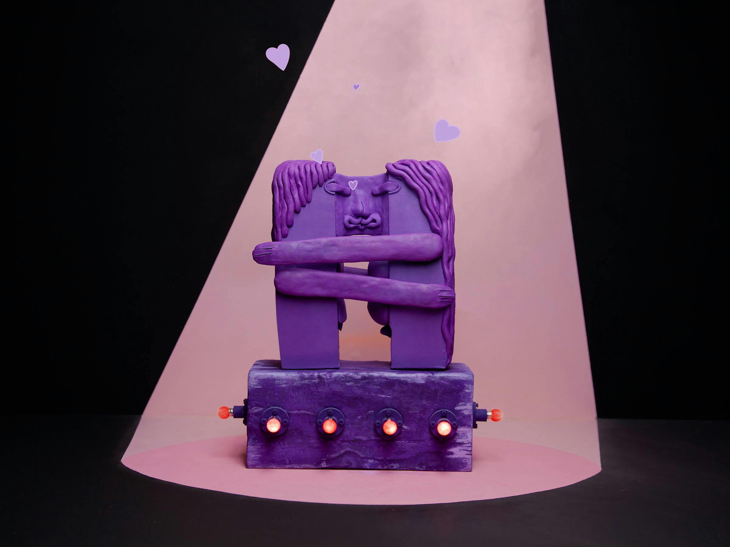 two purple plasticine figures embrace and kiss in a pink spotlight. They are standing on a purple has that has red light bulbs around it 2 purple hearts float above them.