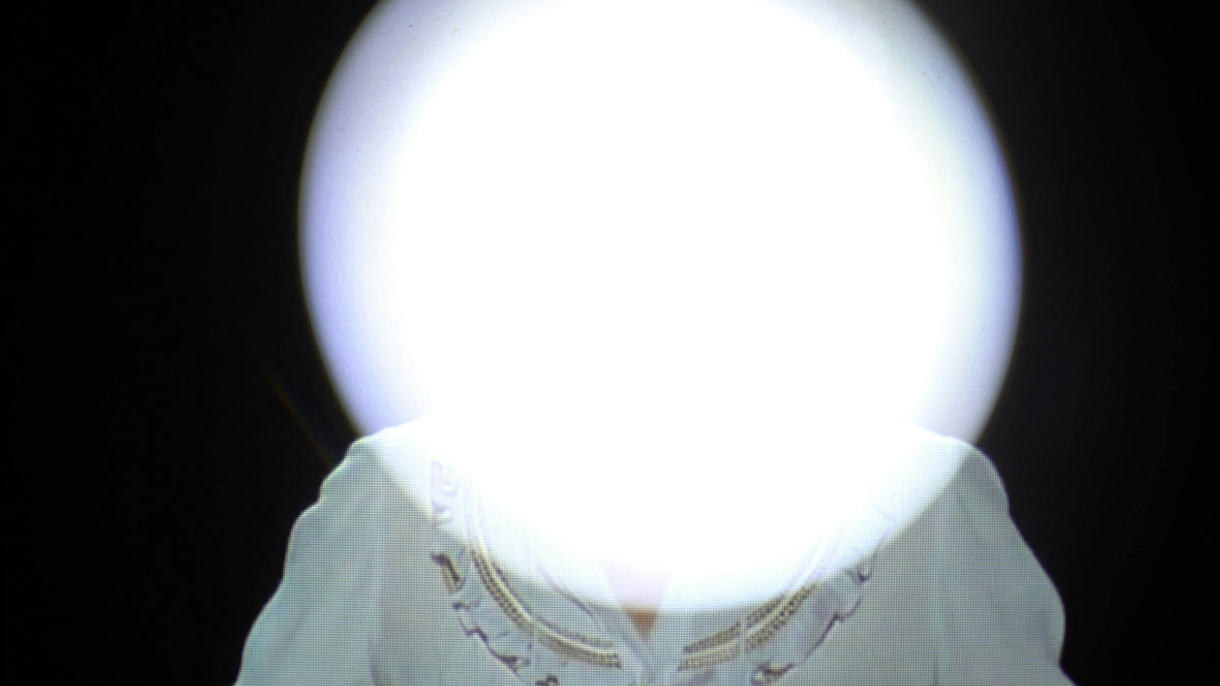 an image of a person wearing a blue blouse. Their face is obscured by a white circle of light. The background is black
