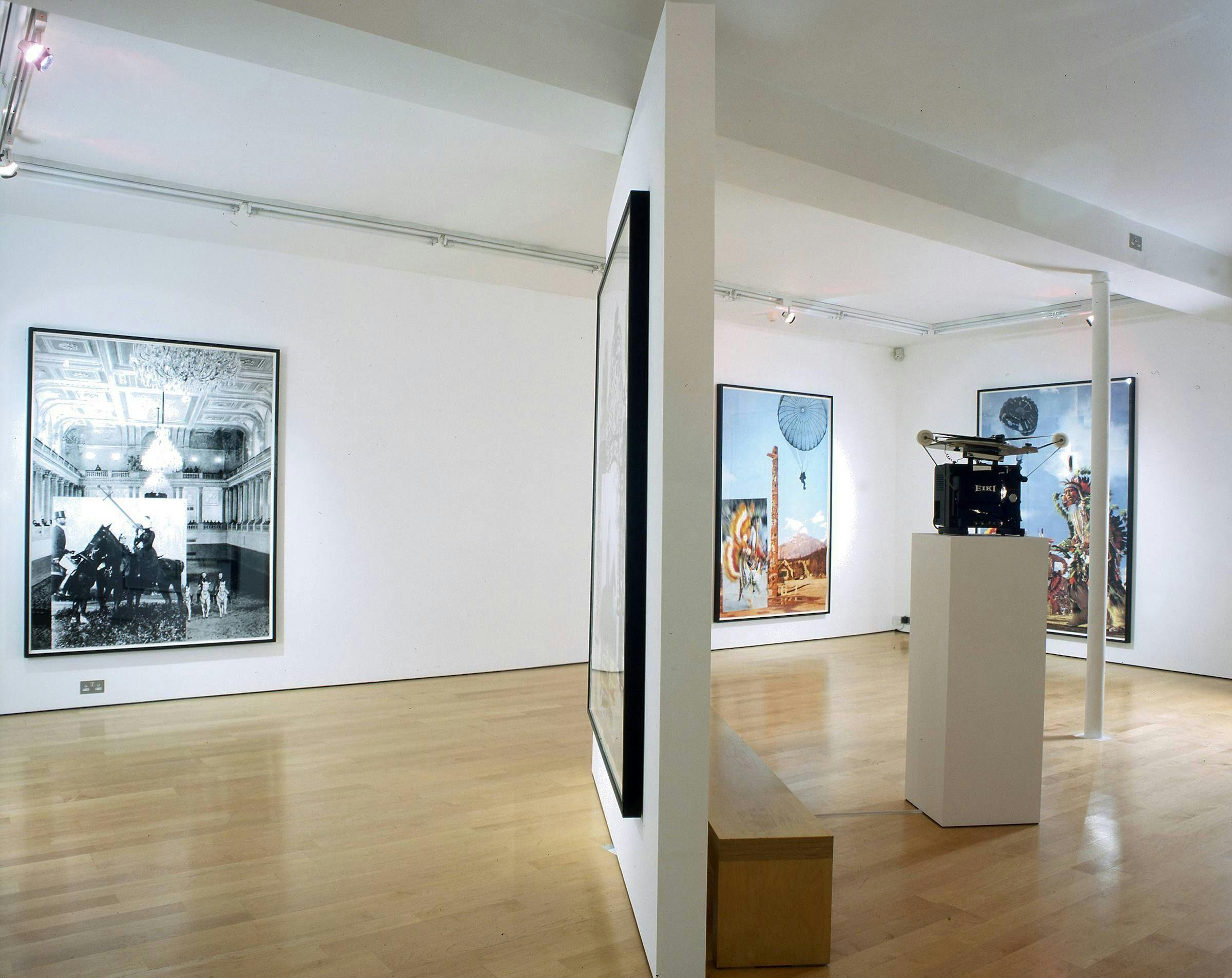 Image of a gallery where four large artworks hand on the walls, there is a bench, and an object sits on top a plinth