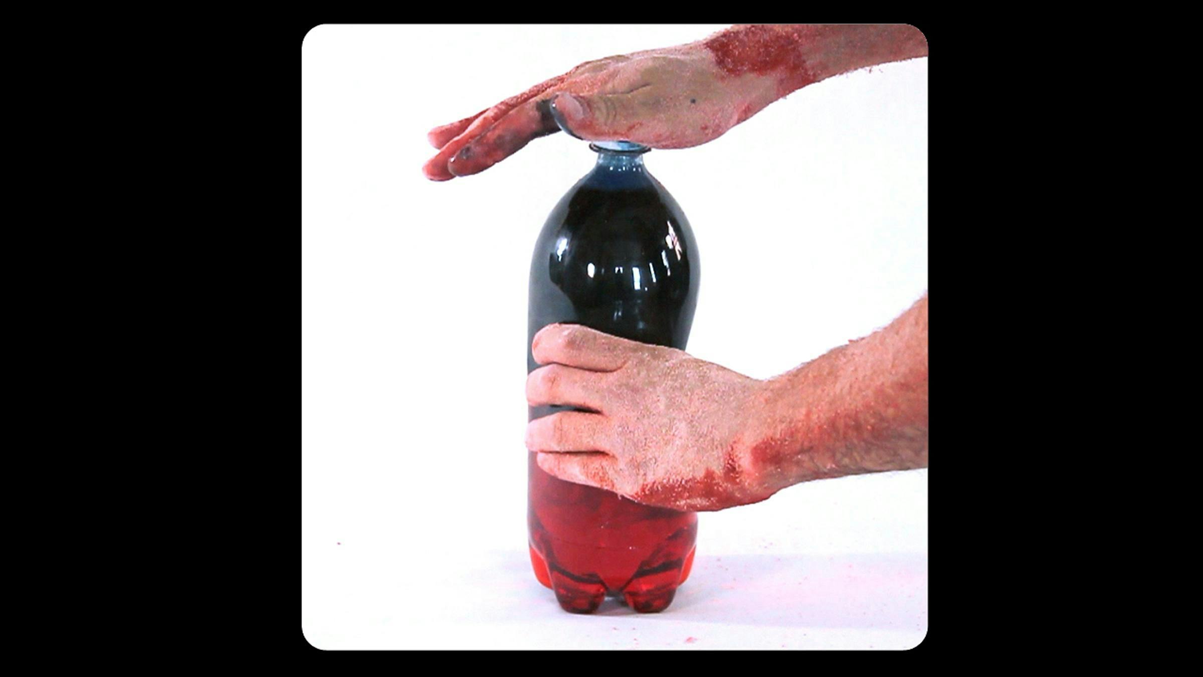 Two hands with red markings on them hold onto a bottle of deep red liquid.