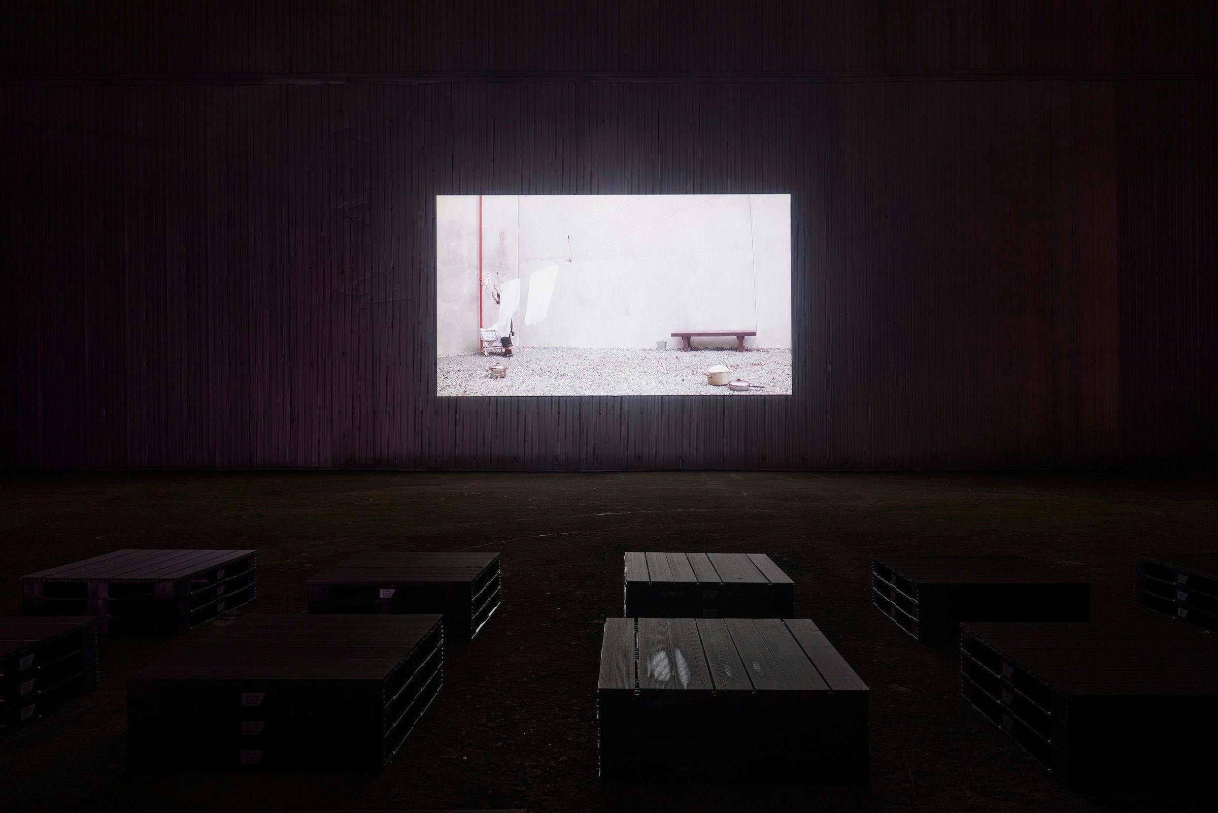 an installation of a video projection in an art gallery. The walls and floor are brown and there are a number of plan chest draws in front of the projector