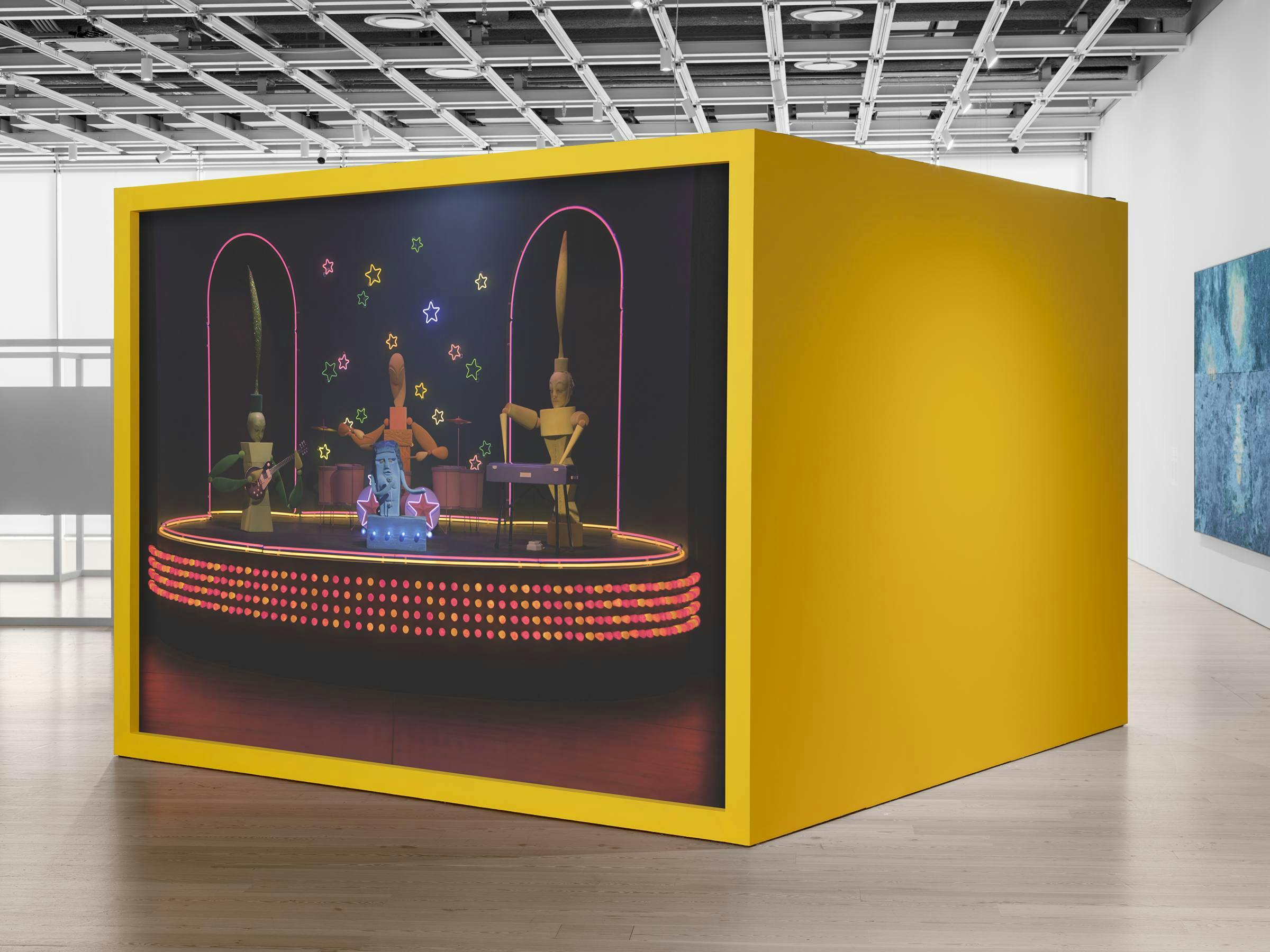an art gallery with wooden floors and white walls. A video art work projected on to a yellow freestanding box. 