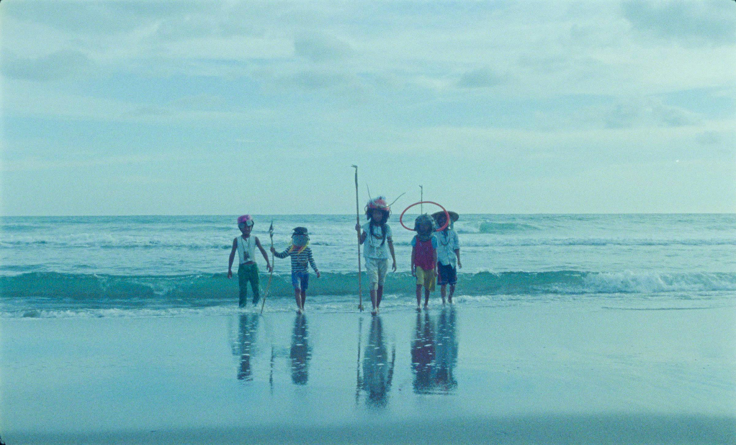 5 figures carrying home made fishing spears walk out of the ocean and towards the camera  in Bataan in the Philippines.
