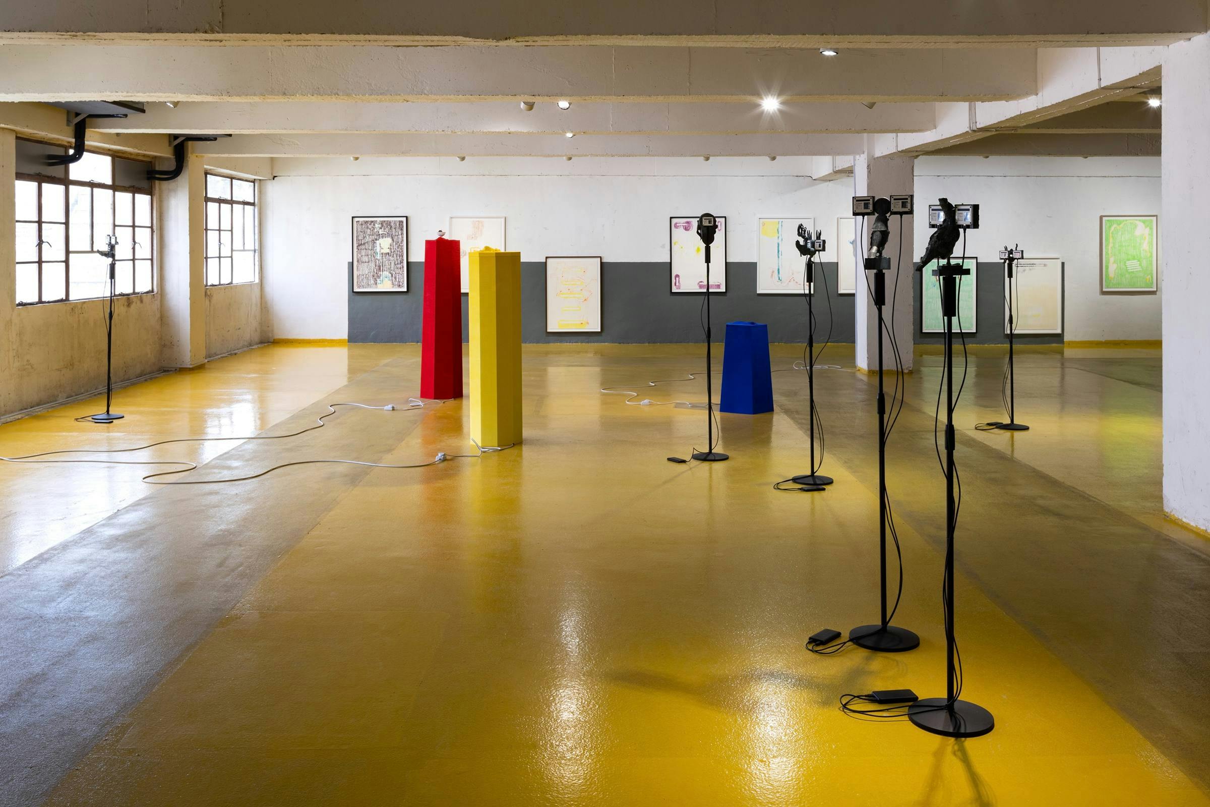 Installation view, Samson Young, The messengers from Music for selective hearing, or assisted living, 24 September - 5 November 2022, Kiang Malingue, Hong Kong. Multiple art works are visible in an industrial space that has a yellow floor