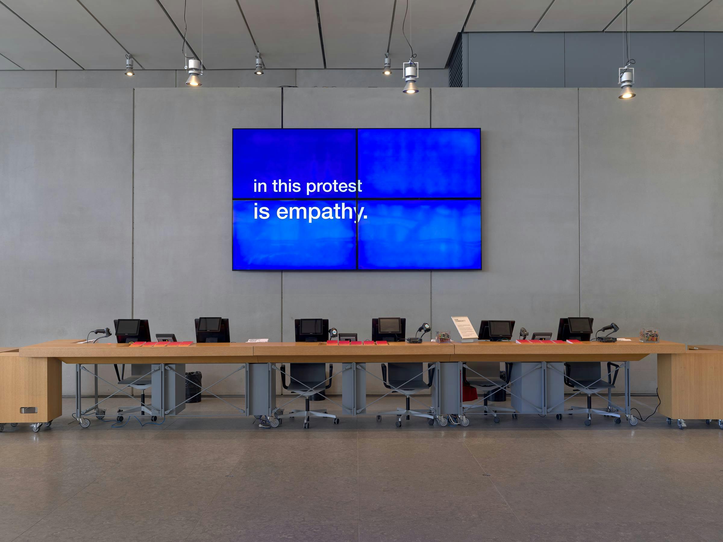Image of a large screen on a grey wall with office desks and chairs in front of it