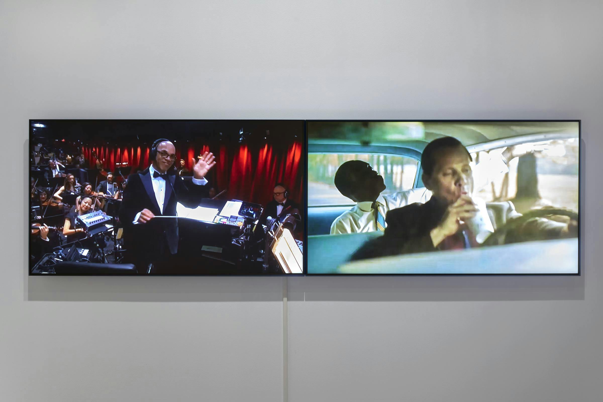 Image of two screens next to one another in a gallery space, each showing a different image. 