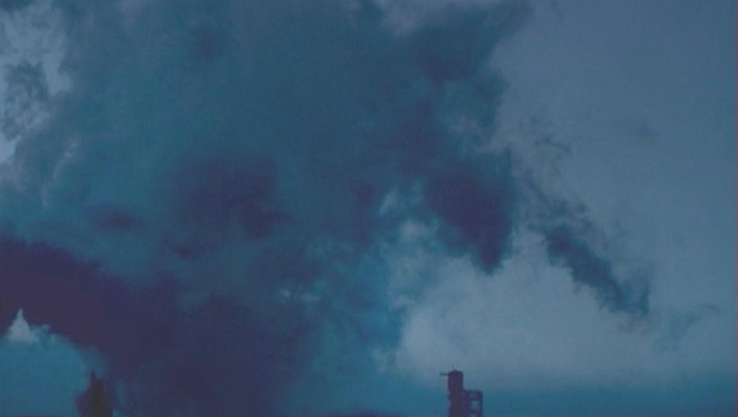 Image of a darkened cloudy sky with dark clouds covering the majority of the image. The top of a chimney is visible in the foreground.