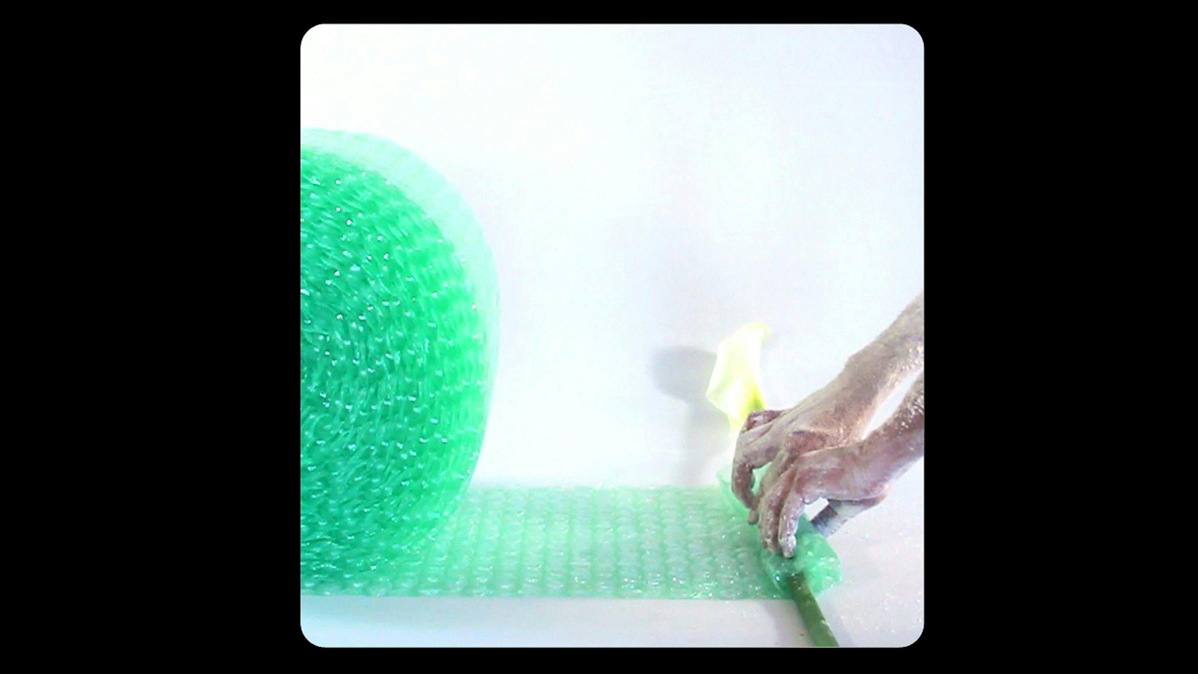 Two hands covered in white power wrap a lily flower stalk in green bubble wrap.