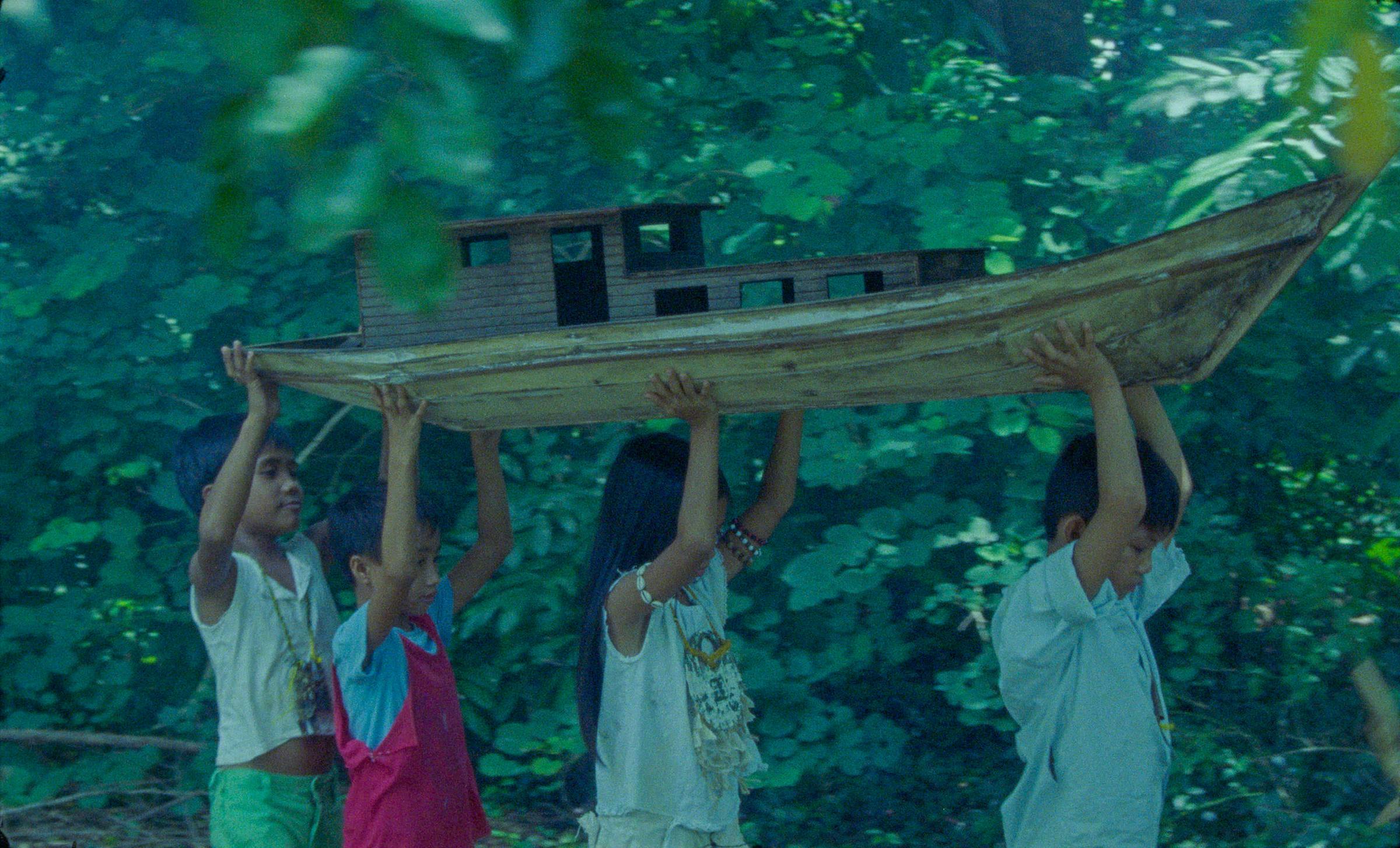4 children carry a wooden boat above their heads in Bataan in the Philippines.
