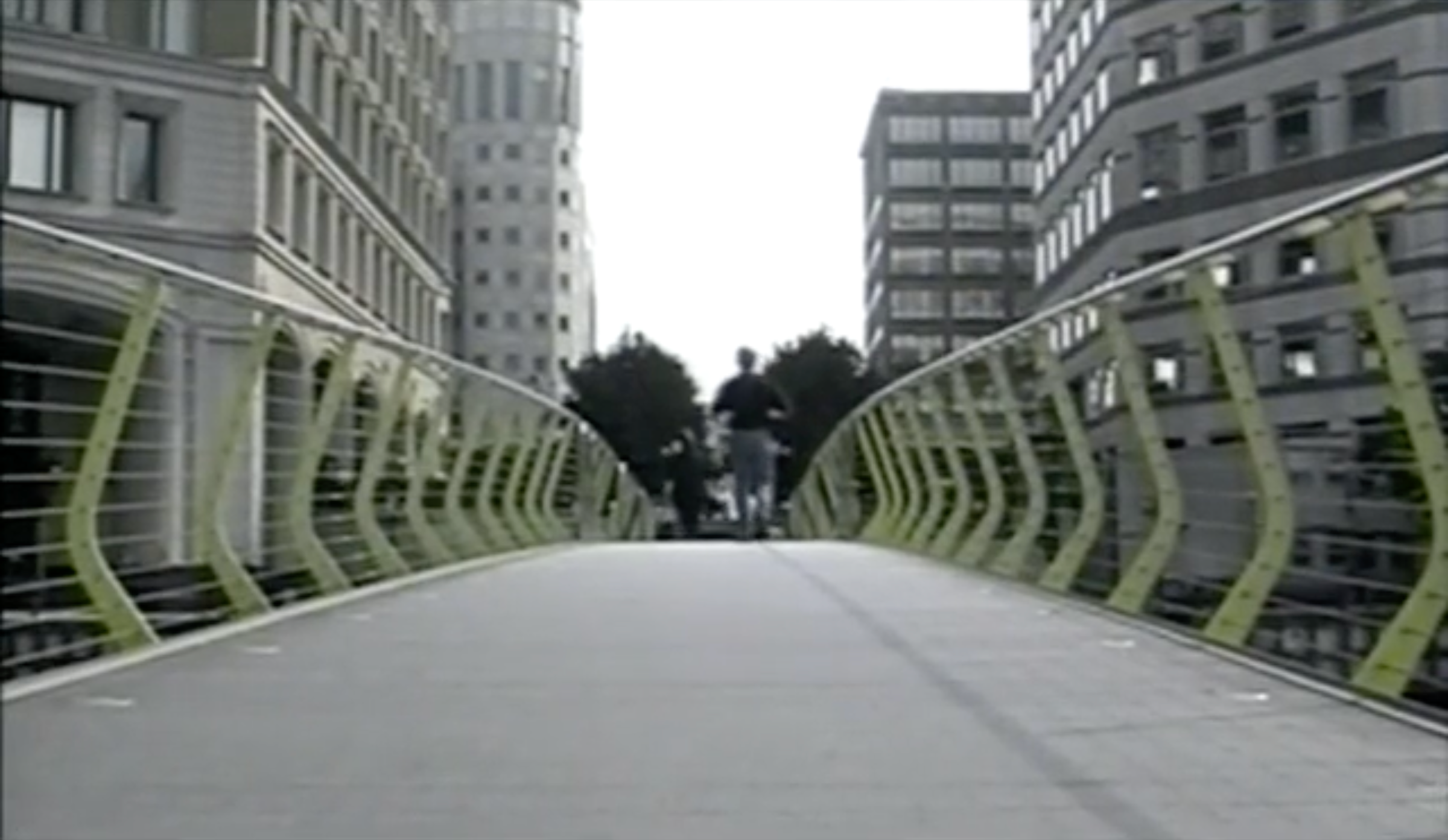 Image taken on a bridge looking across it with a figure running away from the camera and with buildings in the background